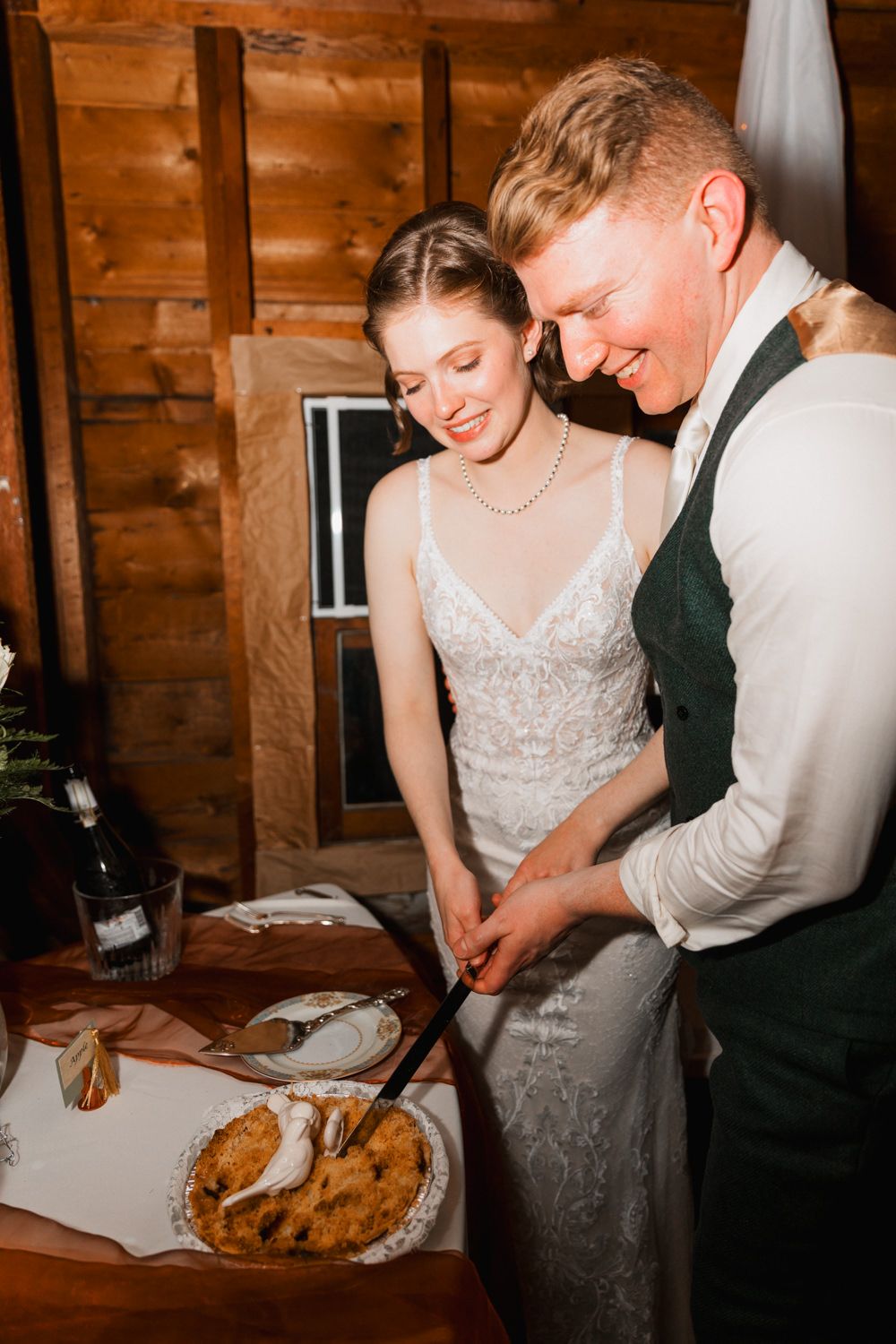 Couple cutting their wedding pie together at rustic wooden reception venue with elegant decor.