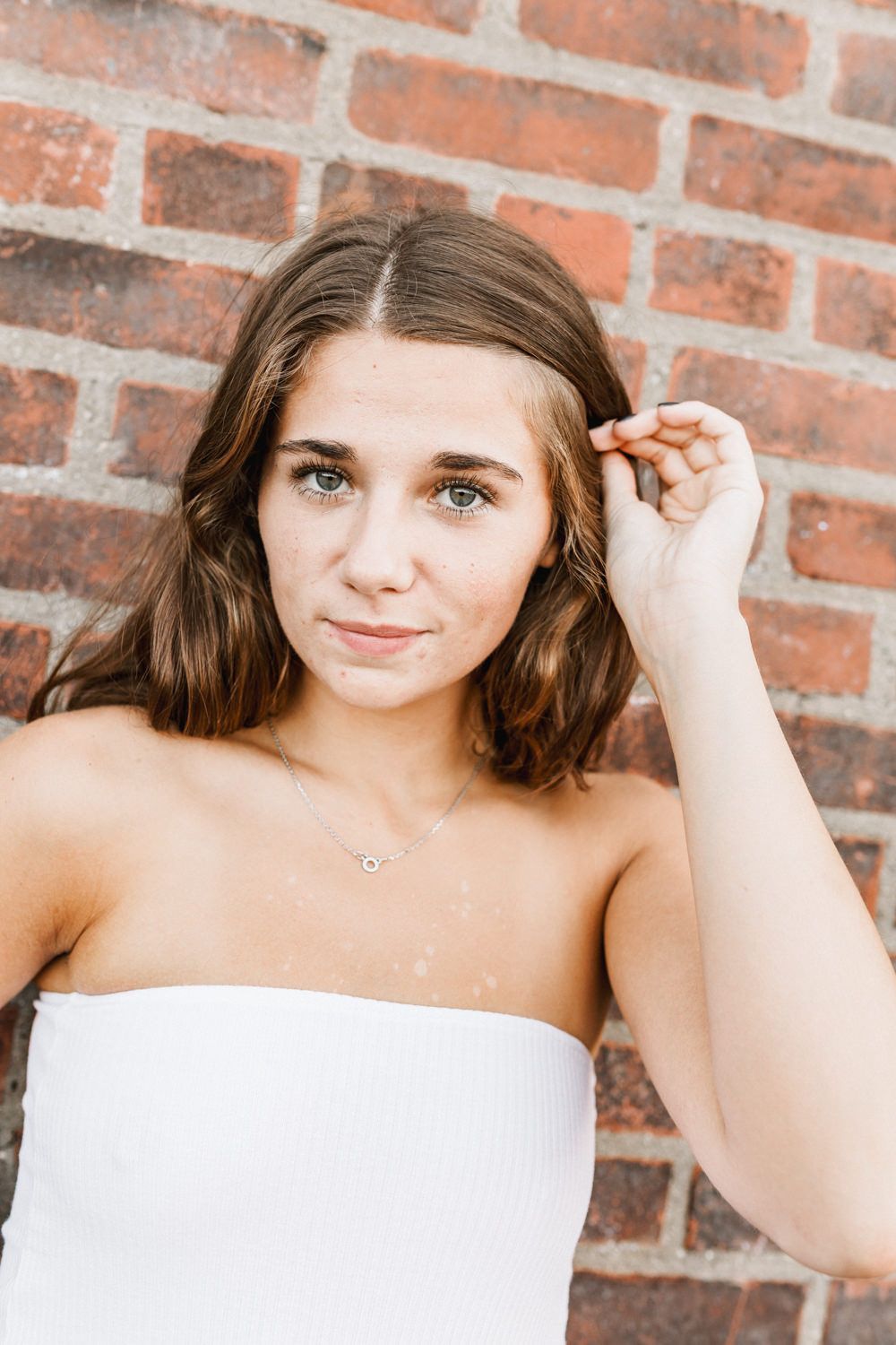 Close-up portrait against brick wall in white strapless top.
