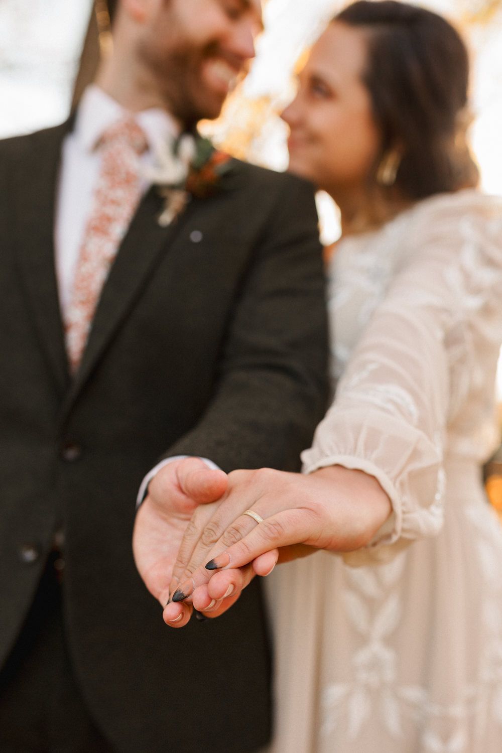 Close-up of hands exchanging wedding rings during a marriage ceremony with soft lighting and elegant attire.