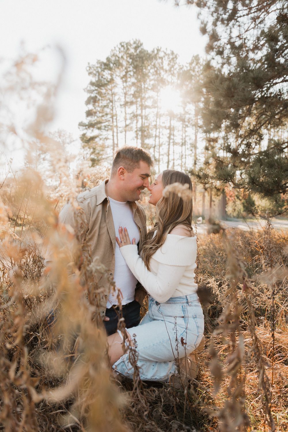 A romantic couple shares intimate moments among golden sunlit trees and dried winter foliage.