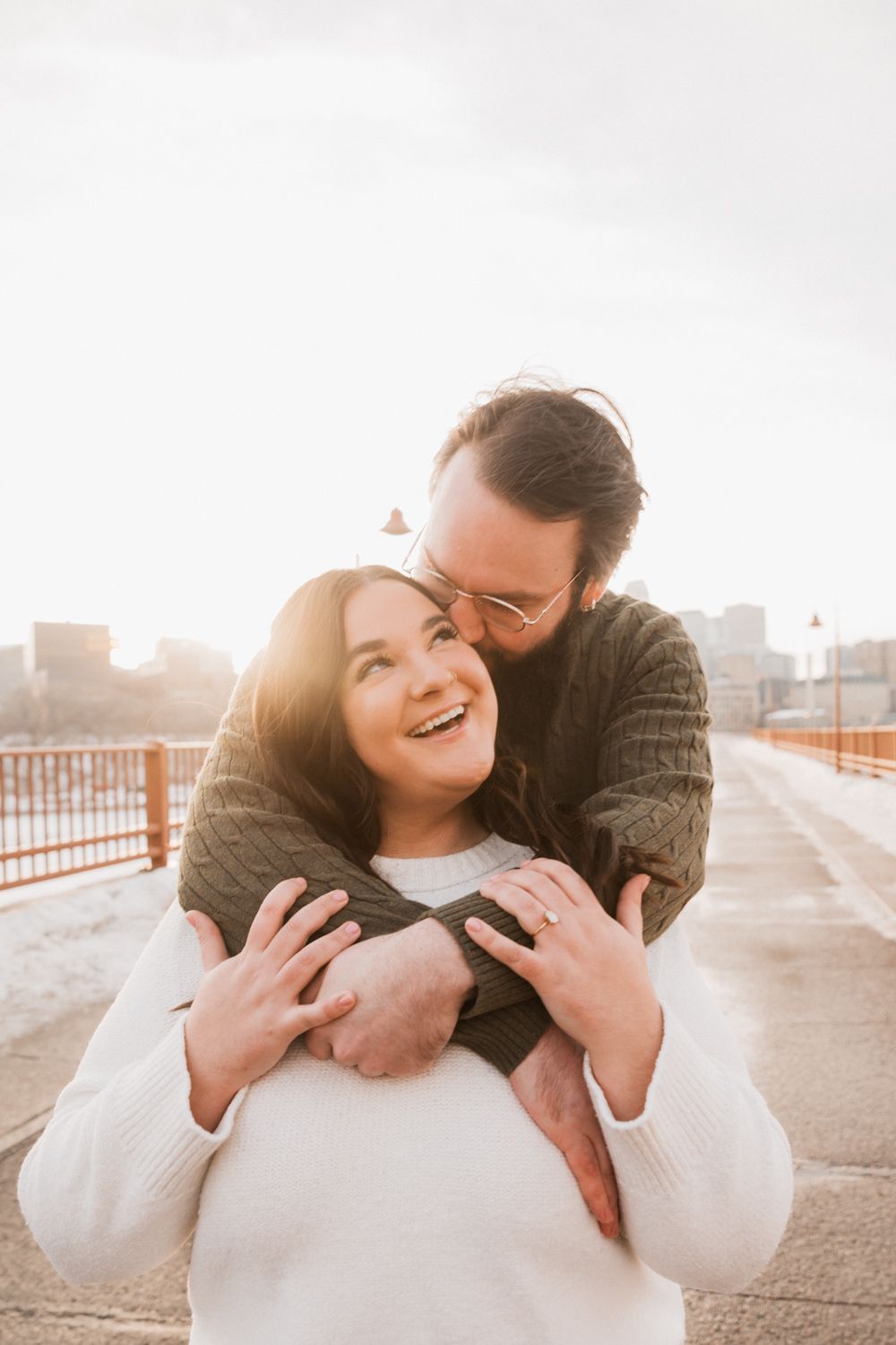 A couple embraces and laughs together on a rooftop during golden hour sunset in an urban setting.
