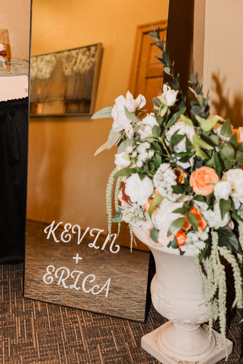 Wedding decor featuring white and peach floral arrangements in vintage urns alongside elegant name displays.