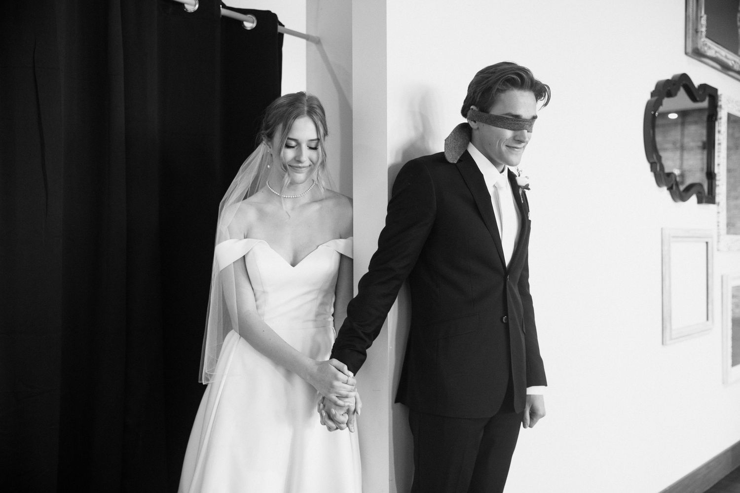 Black and white photo of a bride in a white gown and groom in a tuxedo holding hands at their wedding.