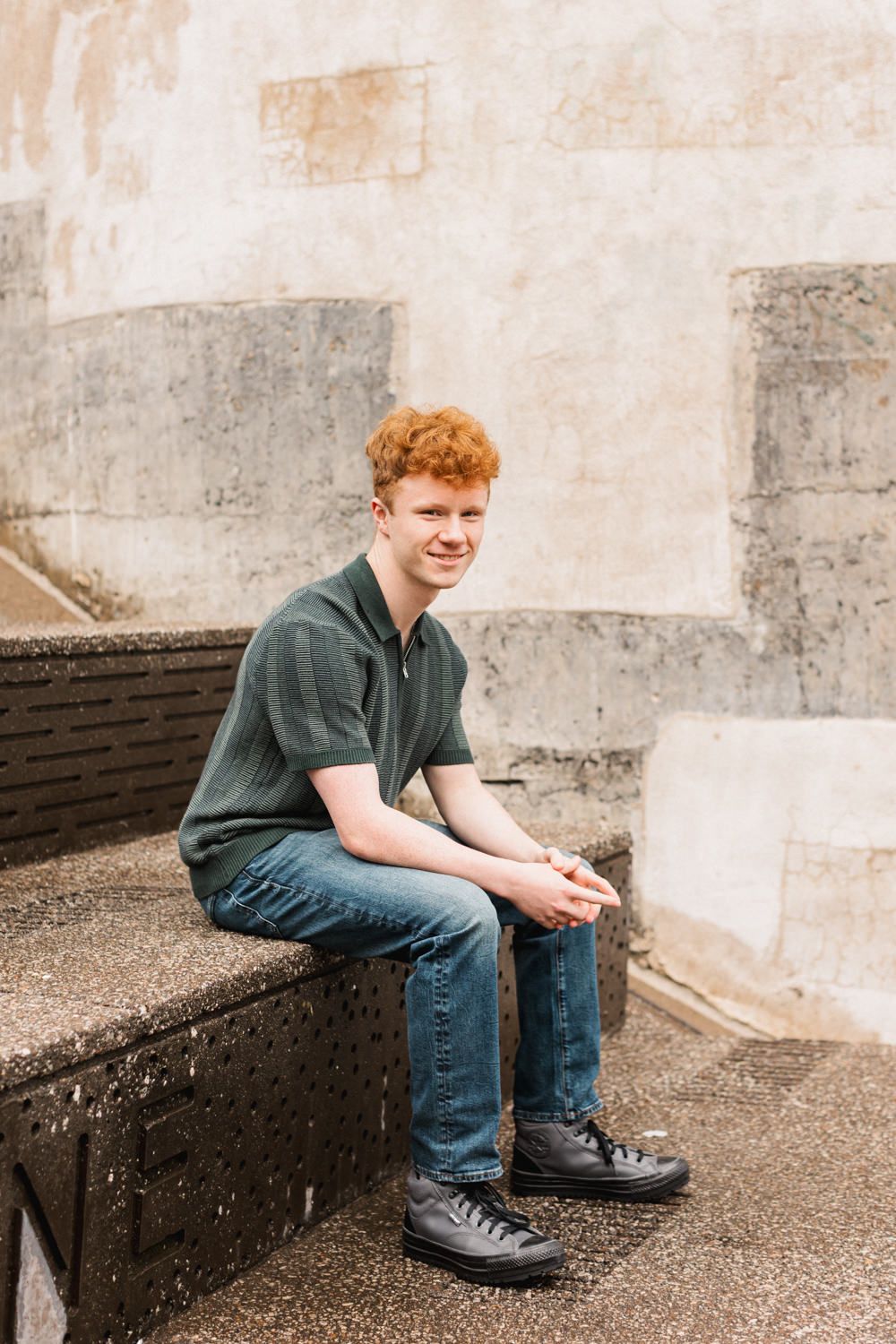 Youth sitting on concrete steps wearing a dark polo shirt and jeans.