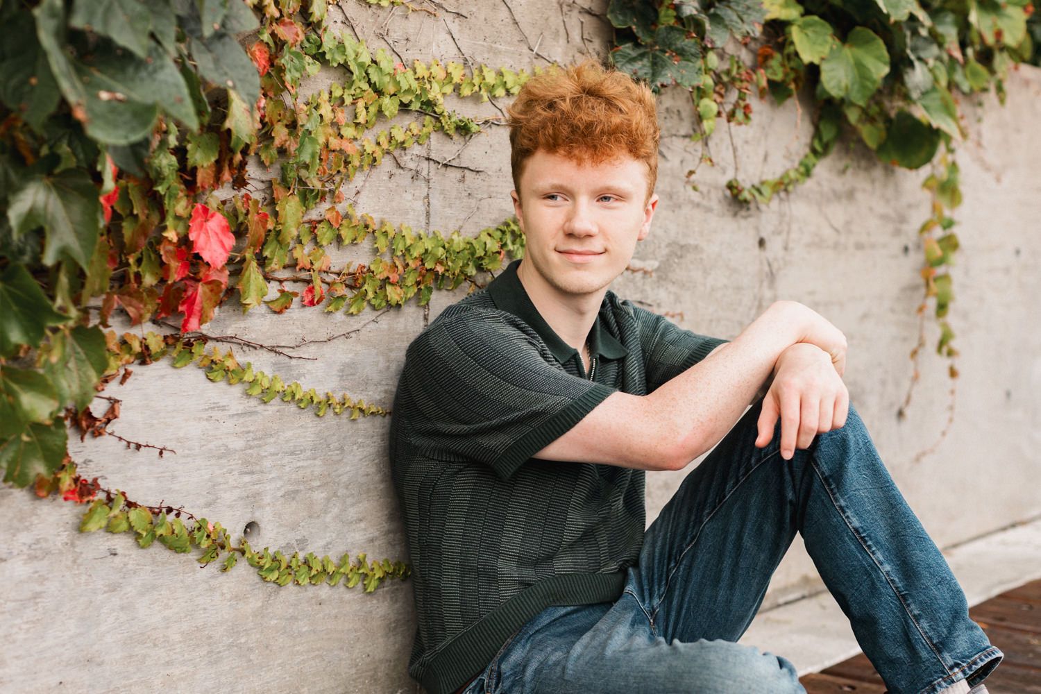 A senior portrait session captured in an outdoor setting with a stone wall and climbing vines in the background.