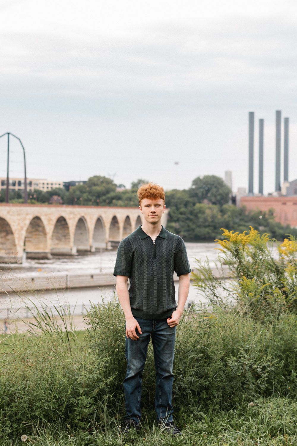 Panoramic view of a stone bridge crossing a river with industrial buildings and chimneys in the background.