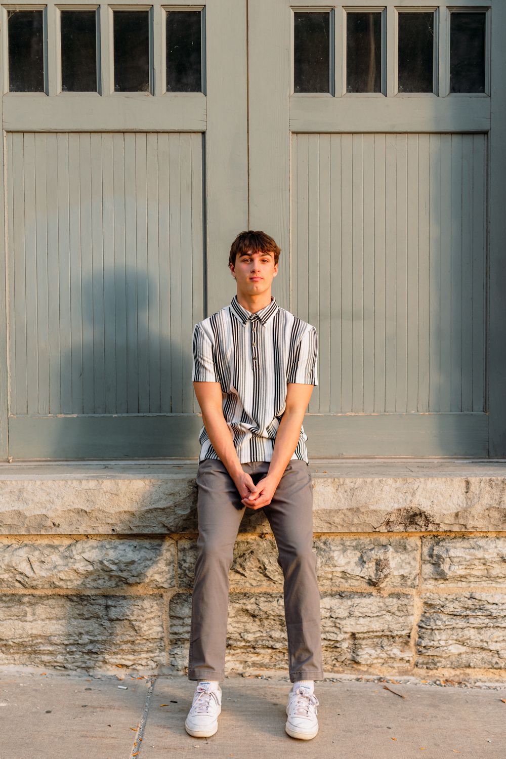 Person sitting on stone ledge against gray building exterior.