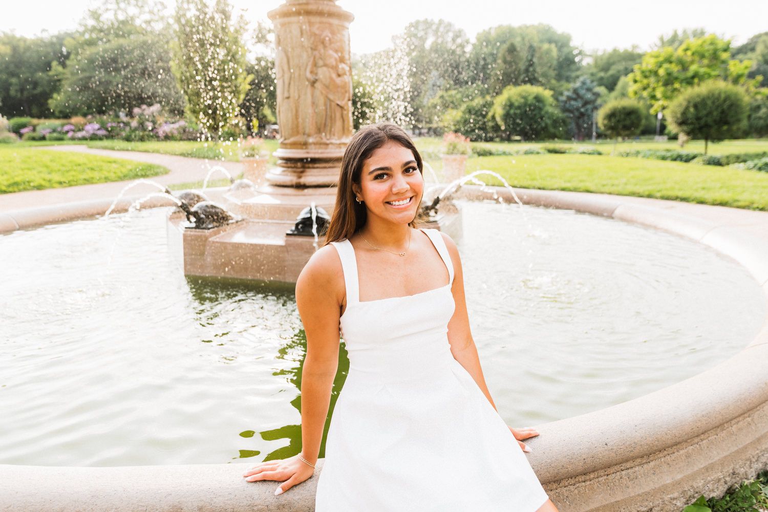 Summer portrait by a decorative water fountain in a sunlit garden setting.