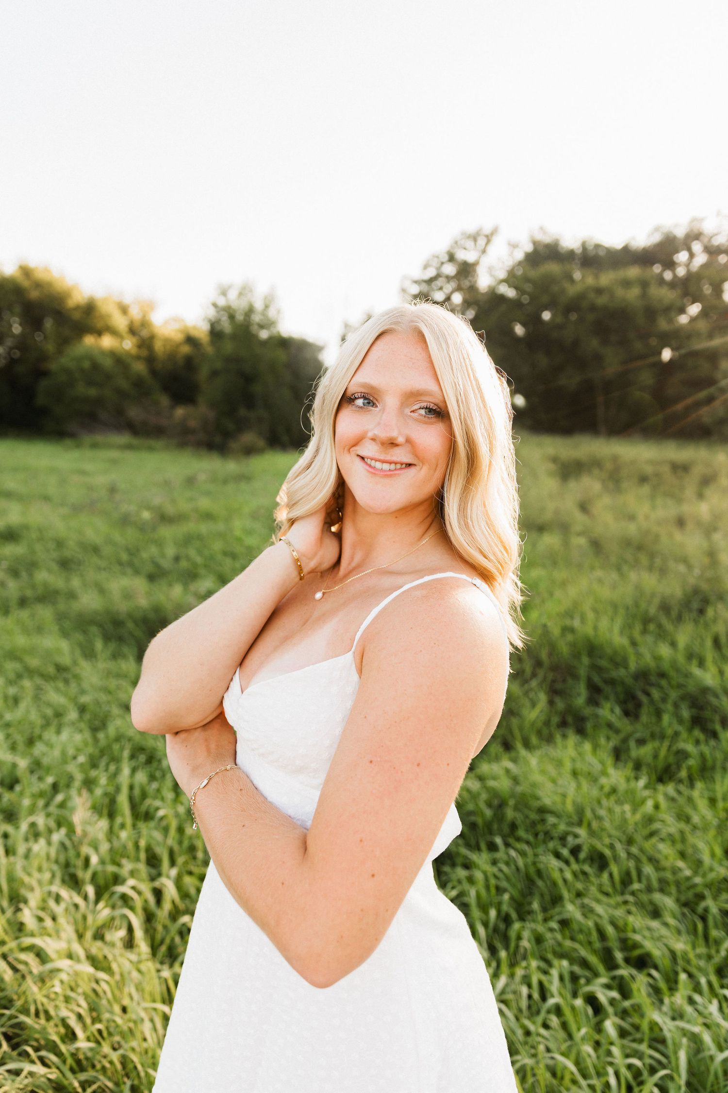 Portrait of someone in a white dress standing in a sunny meadow at golden hour.