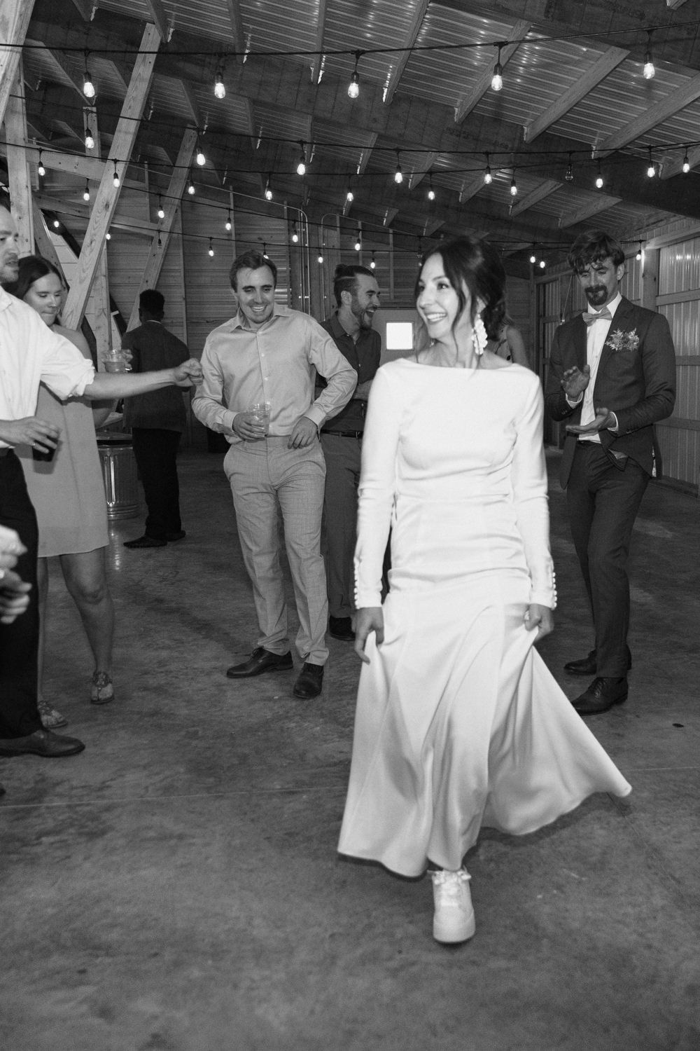 Wedding guests dance in black and white on a concrete floor under string lights.