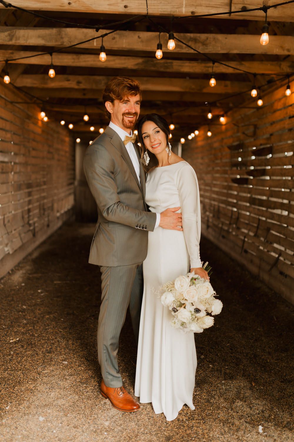 A couple shares romantic moments in a rustic barn setting with string lights creating a warm ambiance.