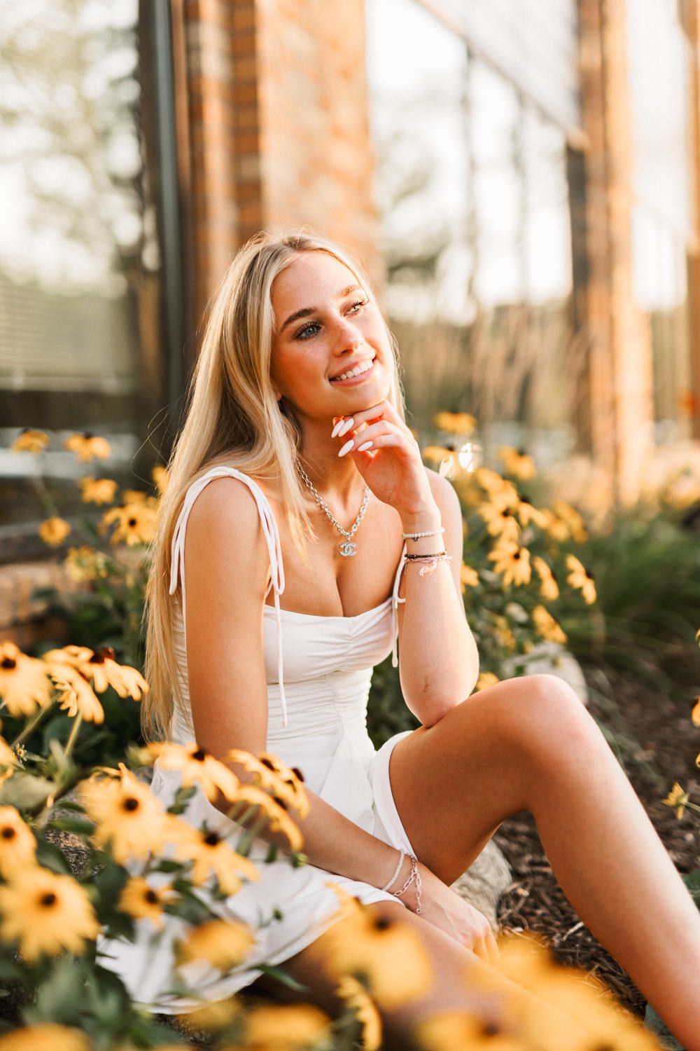 Summer portrait among yellow flowers in white dress at golden hour.