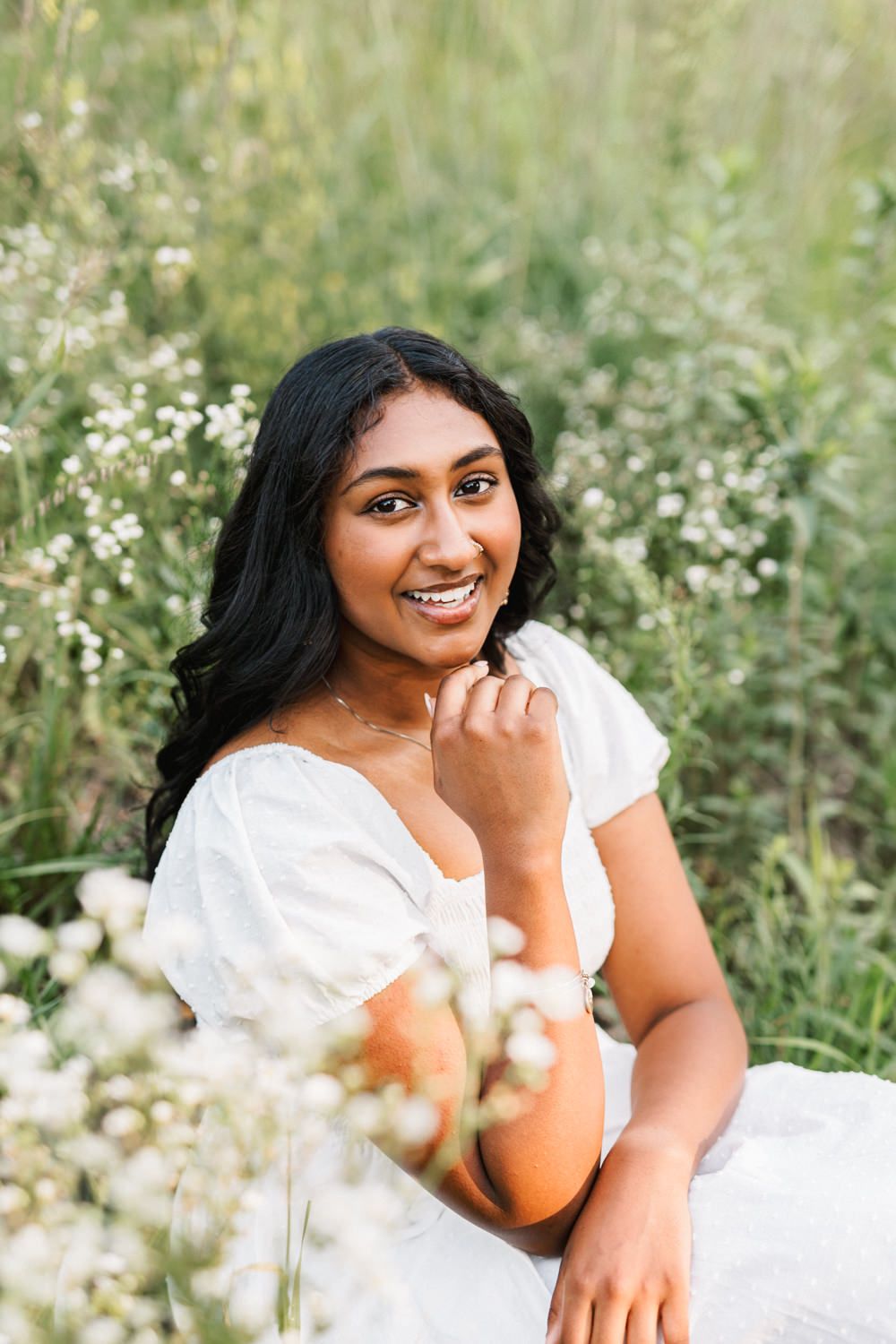 A portrait in a white dress amid delicate wildflowers and natural greenery on a sunny day.
