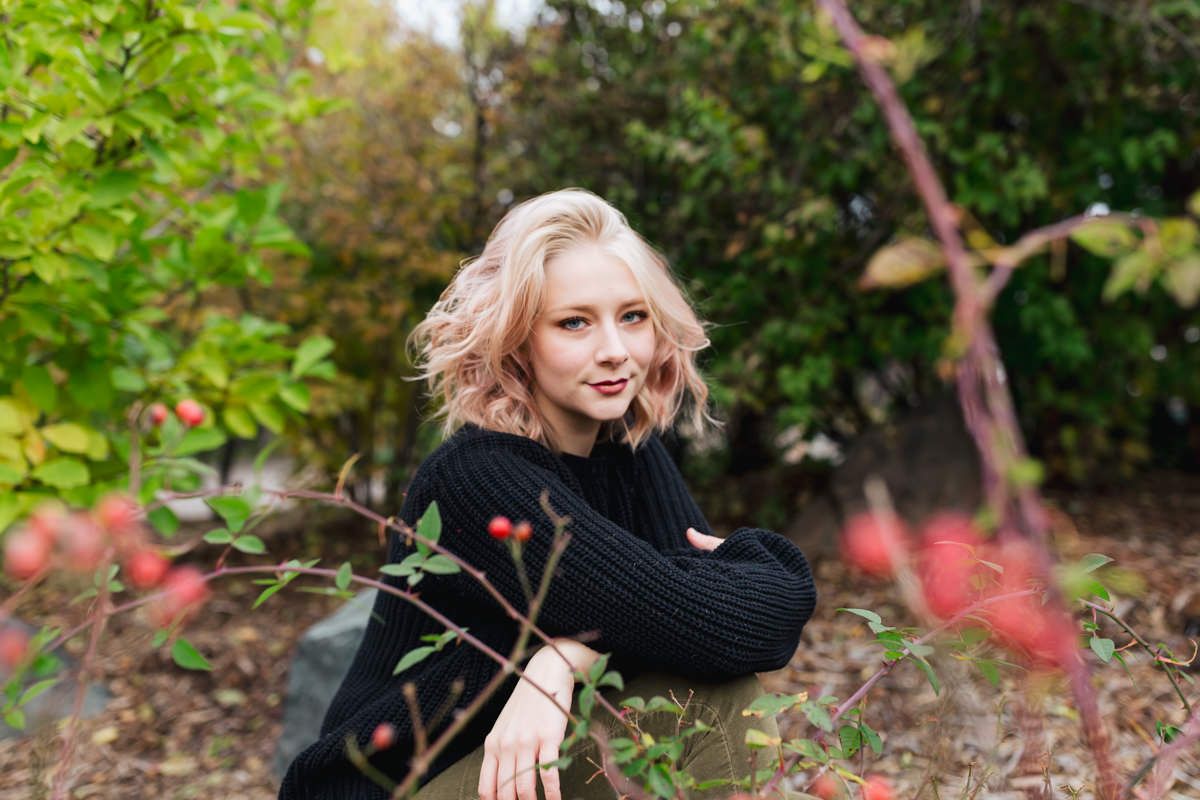Outdoor portrait of person in black sweater posed among autumn foliage.