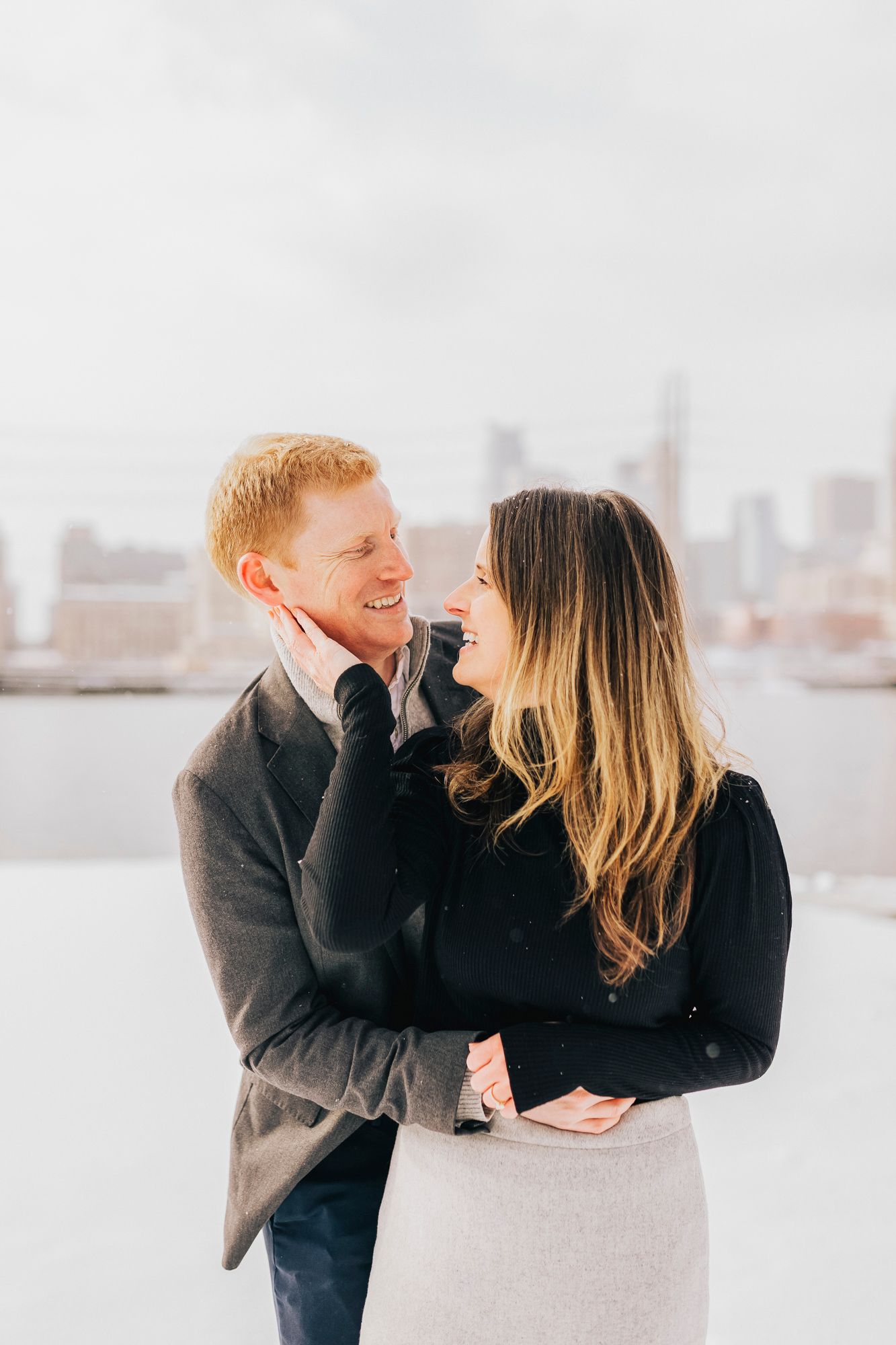 A couple shares a loving moment against a misty winter cityscape backdrop.