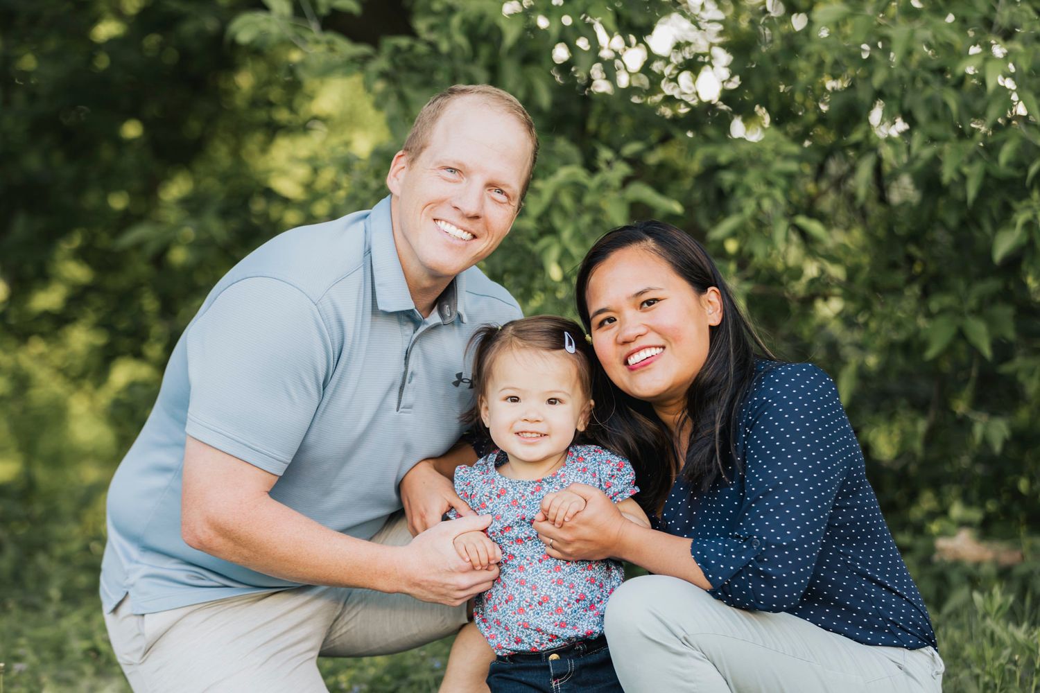 A happy family poses together under flowering tree branches in summer.