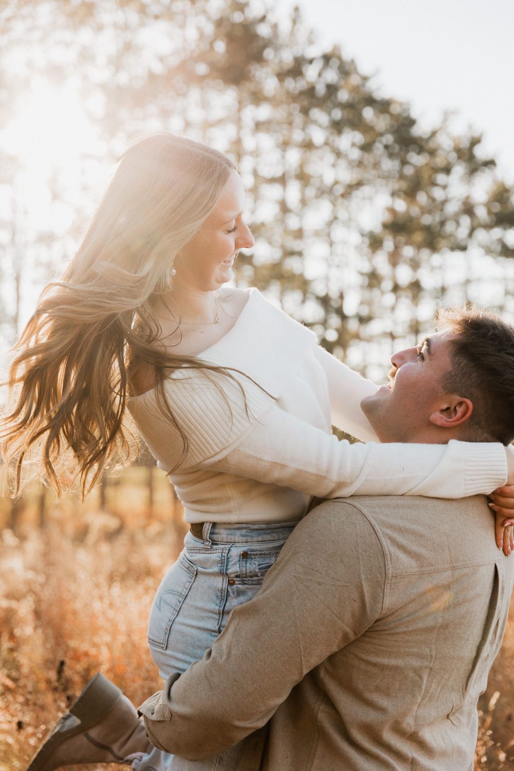 A couple embraces and spins joyfully in a golden-lit field during sunset, creating a romantic autumn moment.