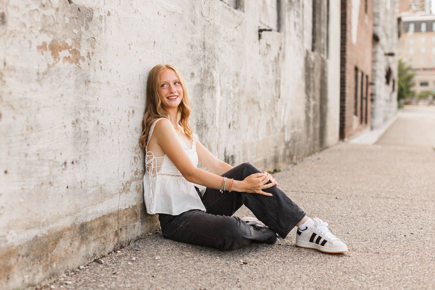 Casual portrait against urban wall wearing white sleeveless top and dark denim.
