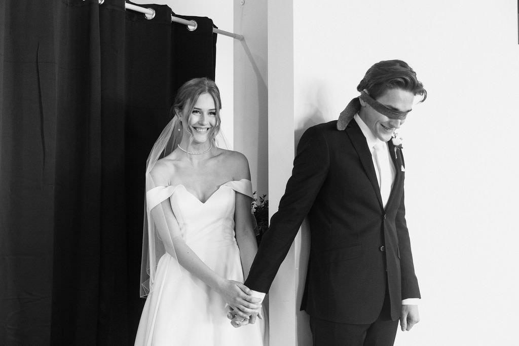 A black and white wedding photo showing a couple holding hands while standing on opposite sides of a wall.