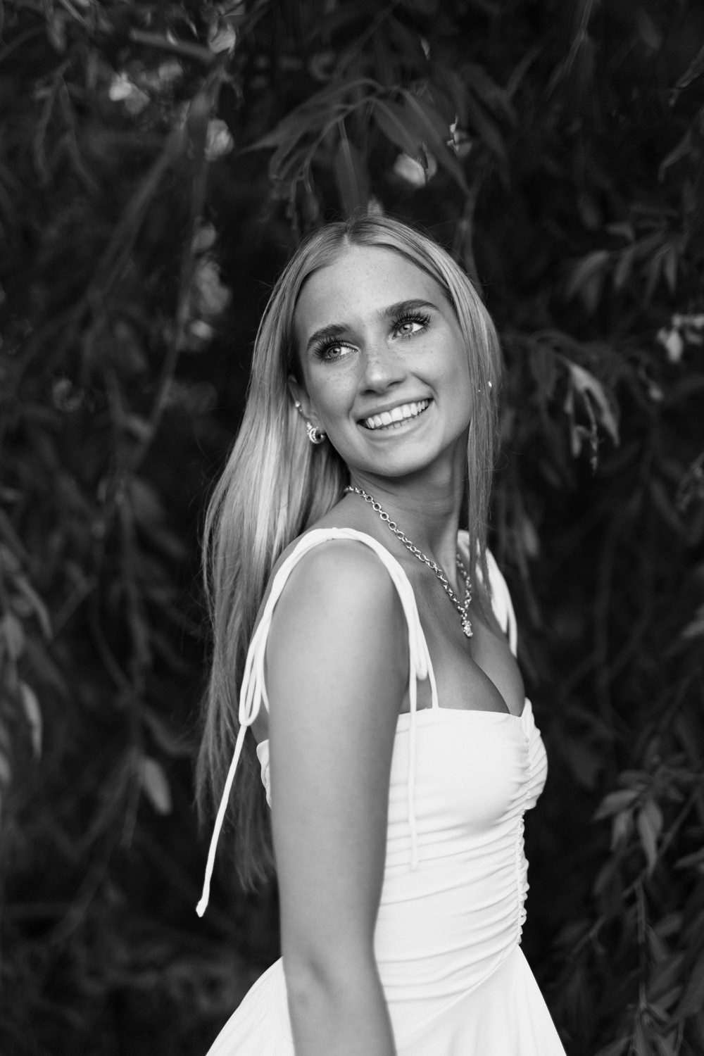 Classic black and white portrait with natural lighting and foliage backdrop.