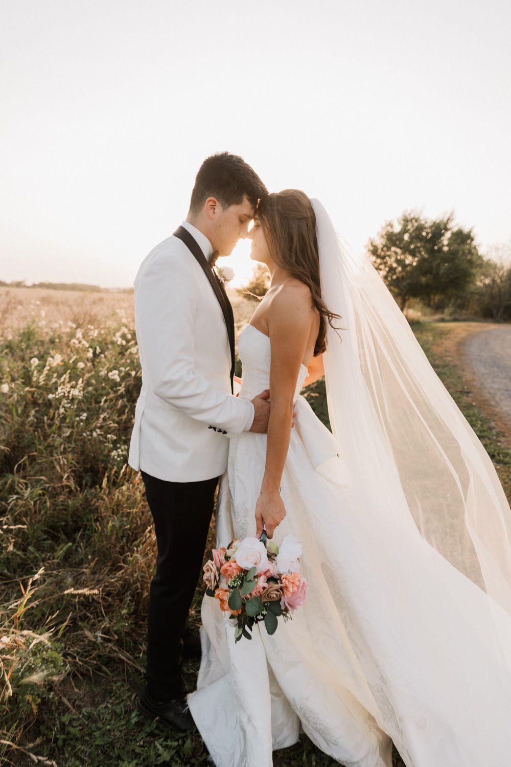 Romantic sunset wedding photos in a field with flowing white dress and bouquet details.