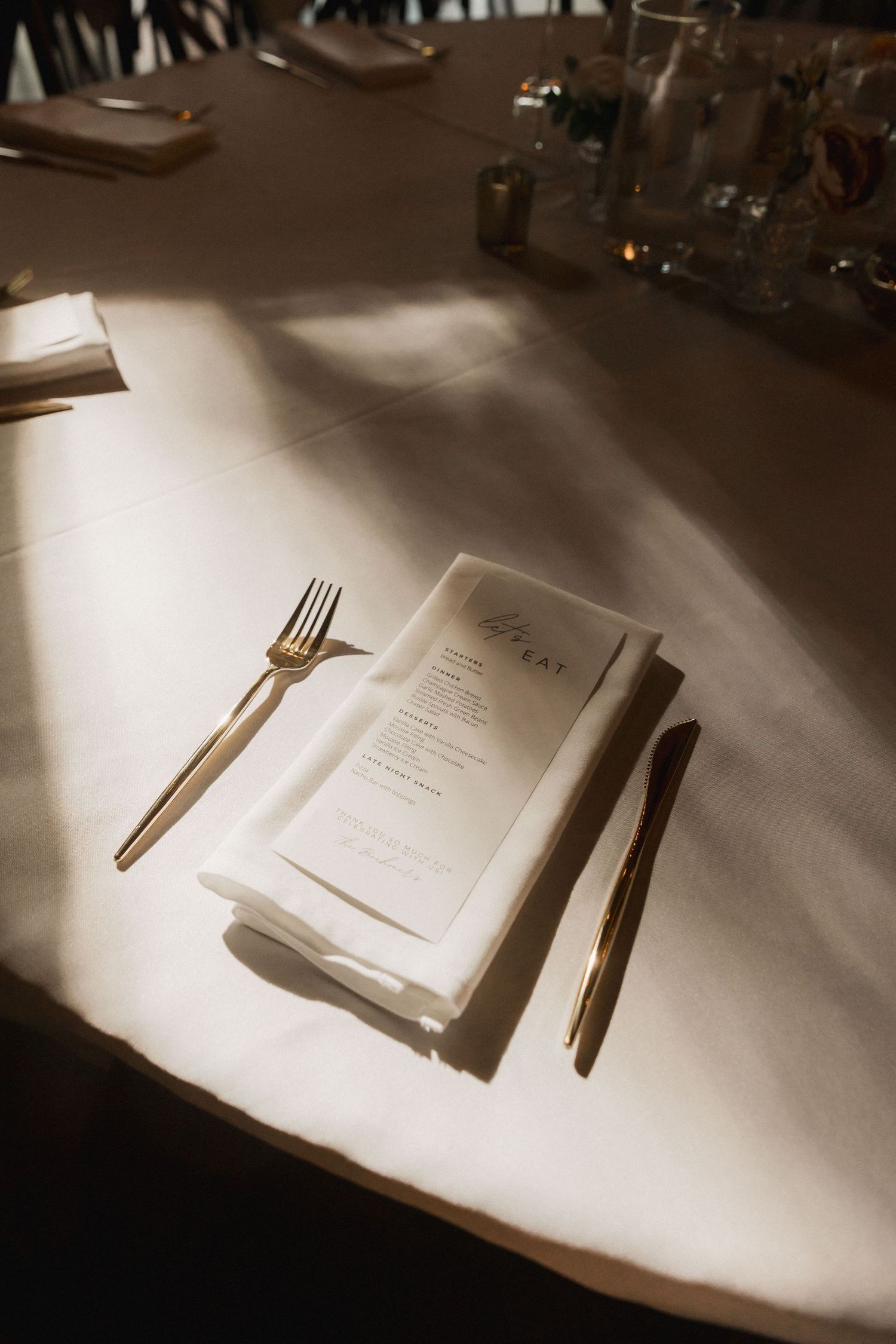 A menu and cutlery on a white tablecloth with dramatic lighting creates an elegant dining atmosphere.