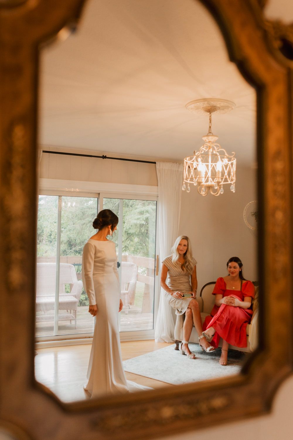 Mirror reflections show a bridal preparation scene with people in white and red dresses in a bright sunlit room.