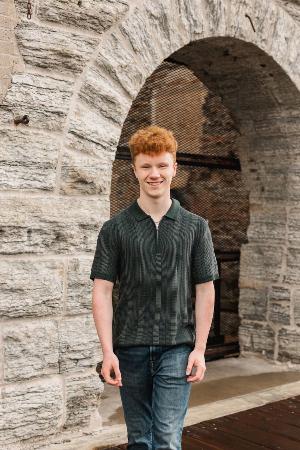 A casual portrait under a stone archway wearing a dark green polo shirt and jeans.