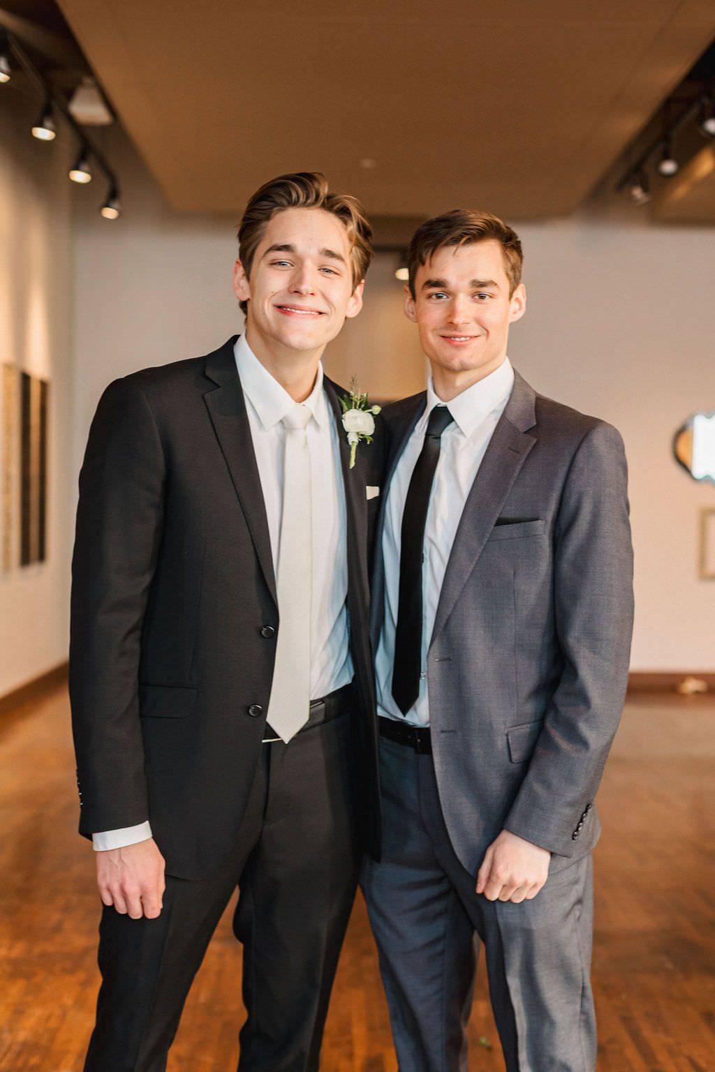 Two men in formal suits pose together in an indoor venue with warm lighting.