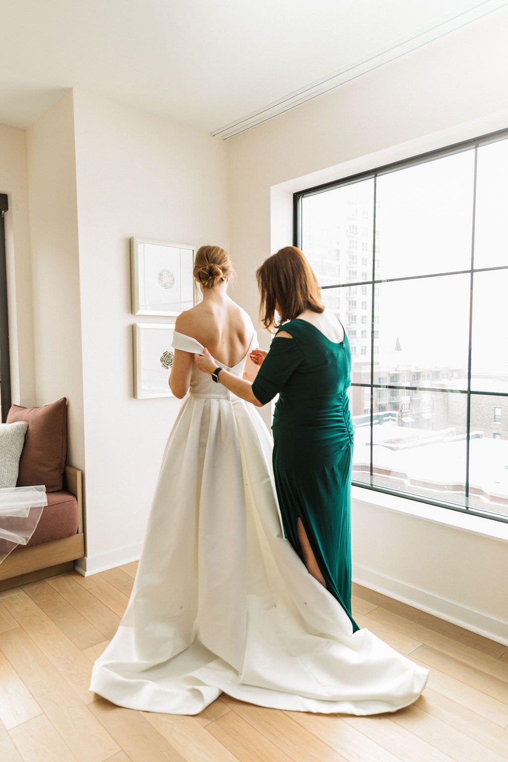 A bride in a classic white ballgown gets final adjustments in a bright modern room.