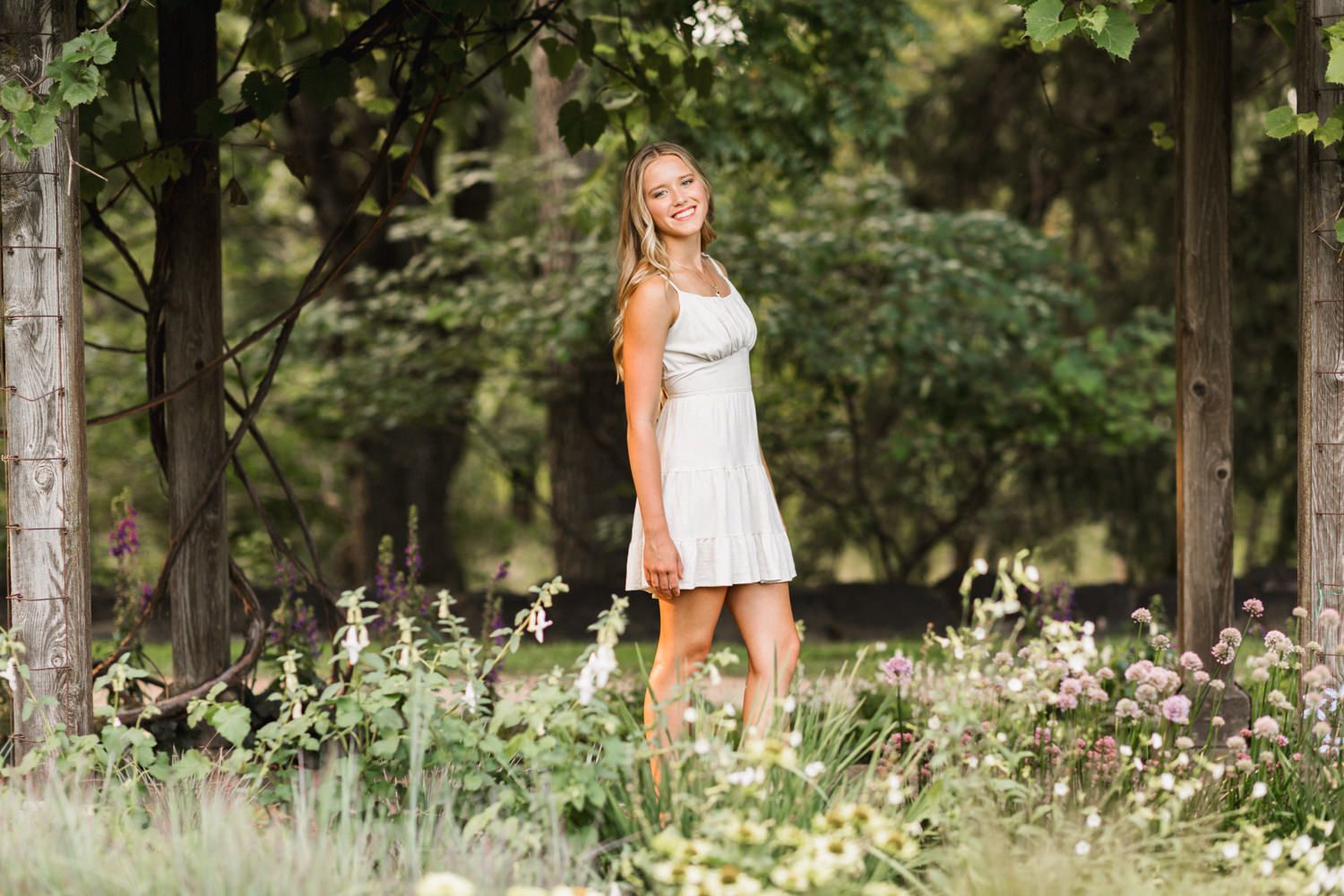 Casual white dress amid wildflowers and trees in a peaceful garden setting.