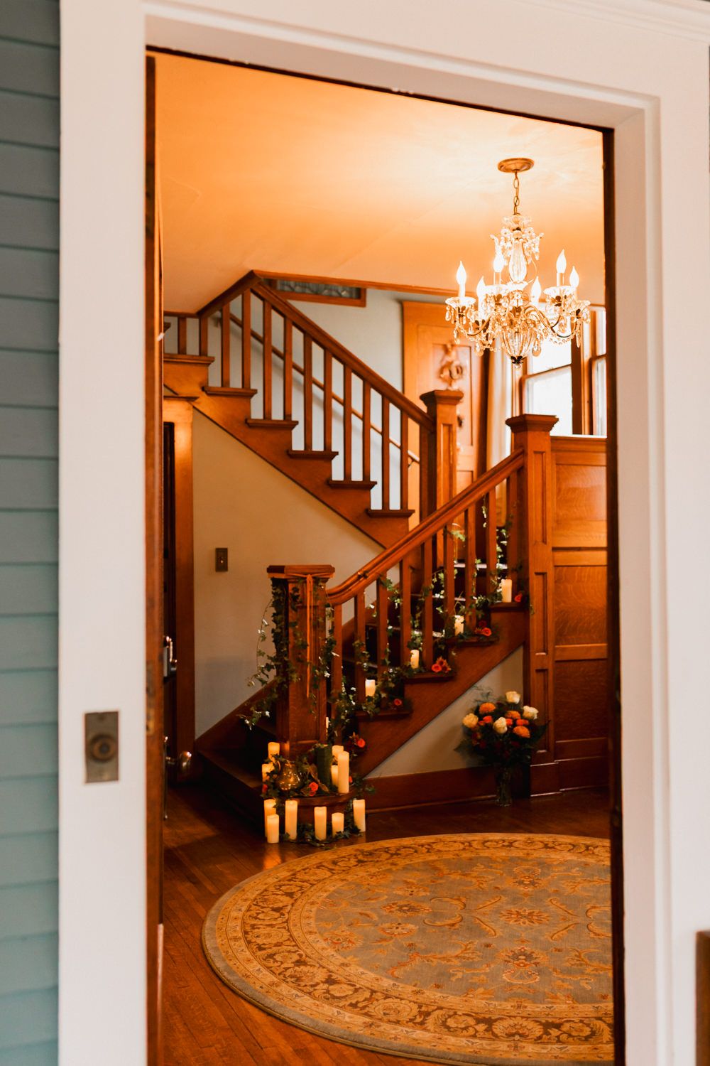 Three illuminated doorways reveal an elegant staircase decorated with candles and holiday greenery.