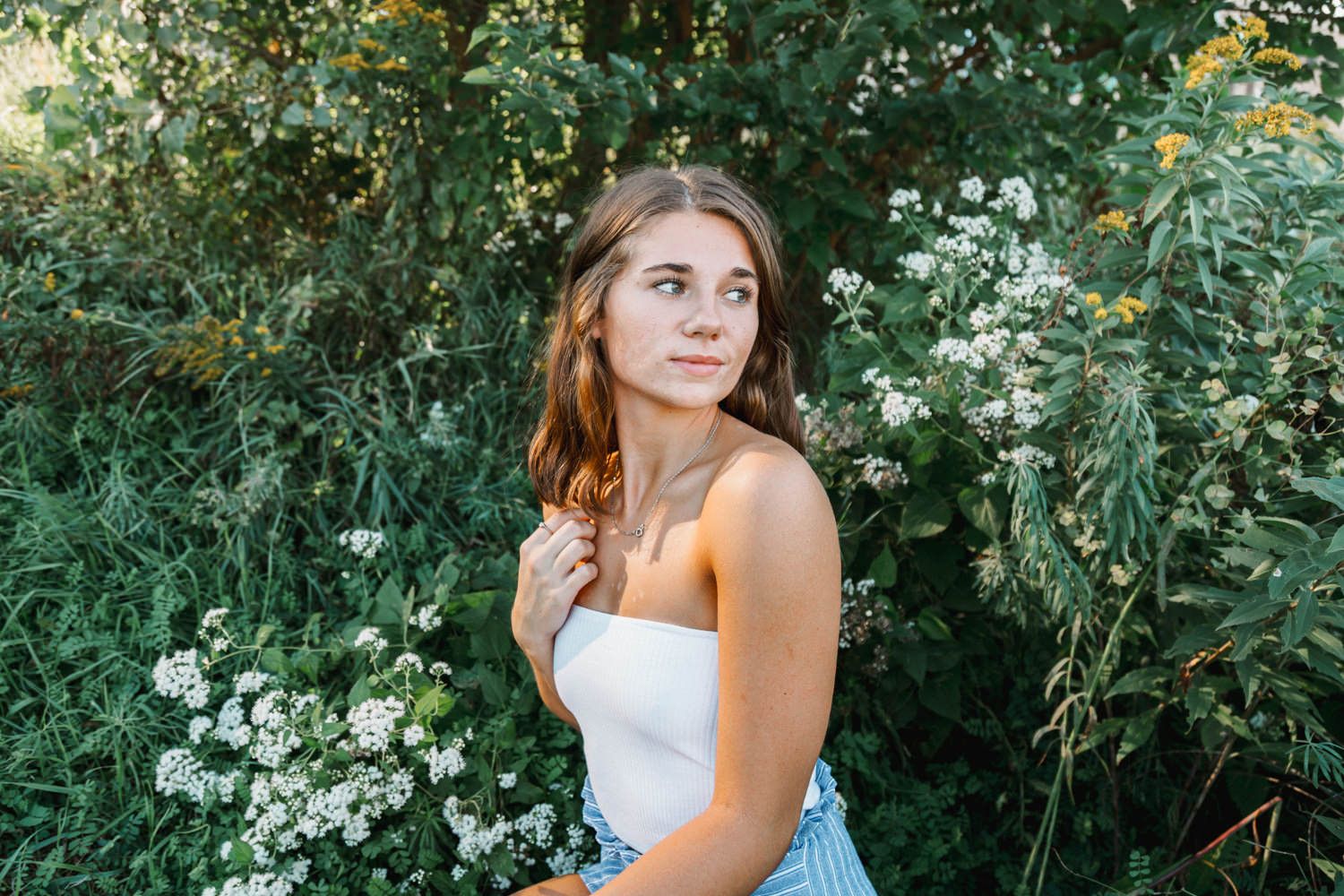 Outdoor portrait in white top surrounded by summer garden flowers.
