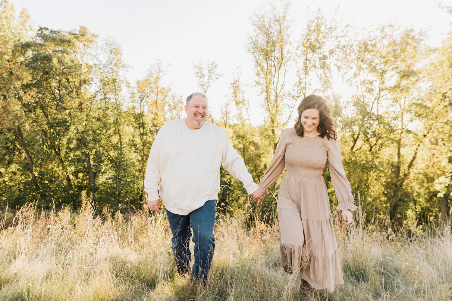 A couple walking hand in hand through a natural setting with golden sunlight filtering through trees.