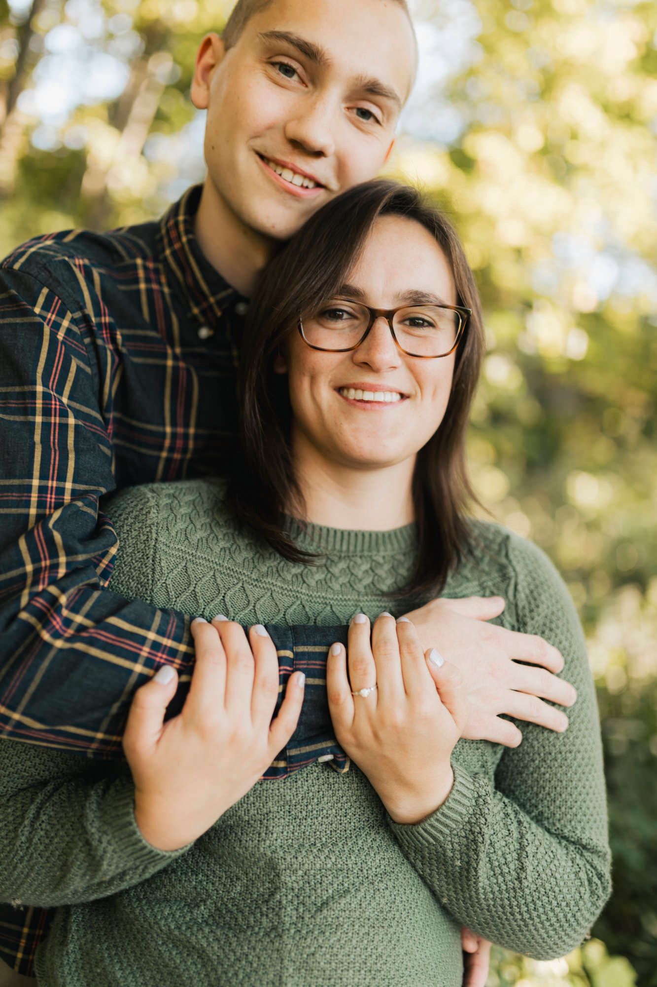 Couple embracing outdoors, wearing casual sweater and plaid shirt.