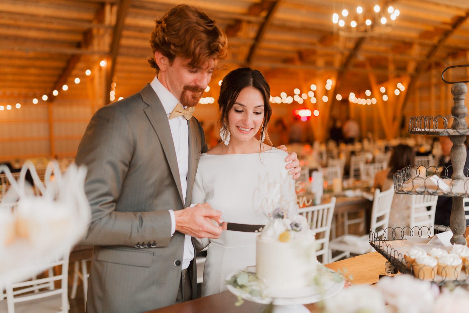 Newlyweds dancing and laughing together during their reception in a warmly lit barn venue.