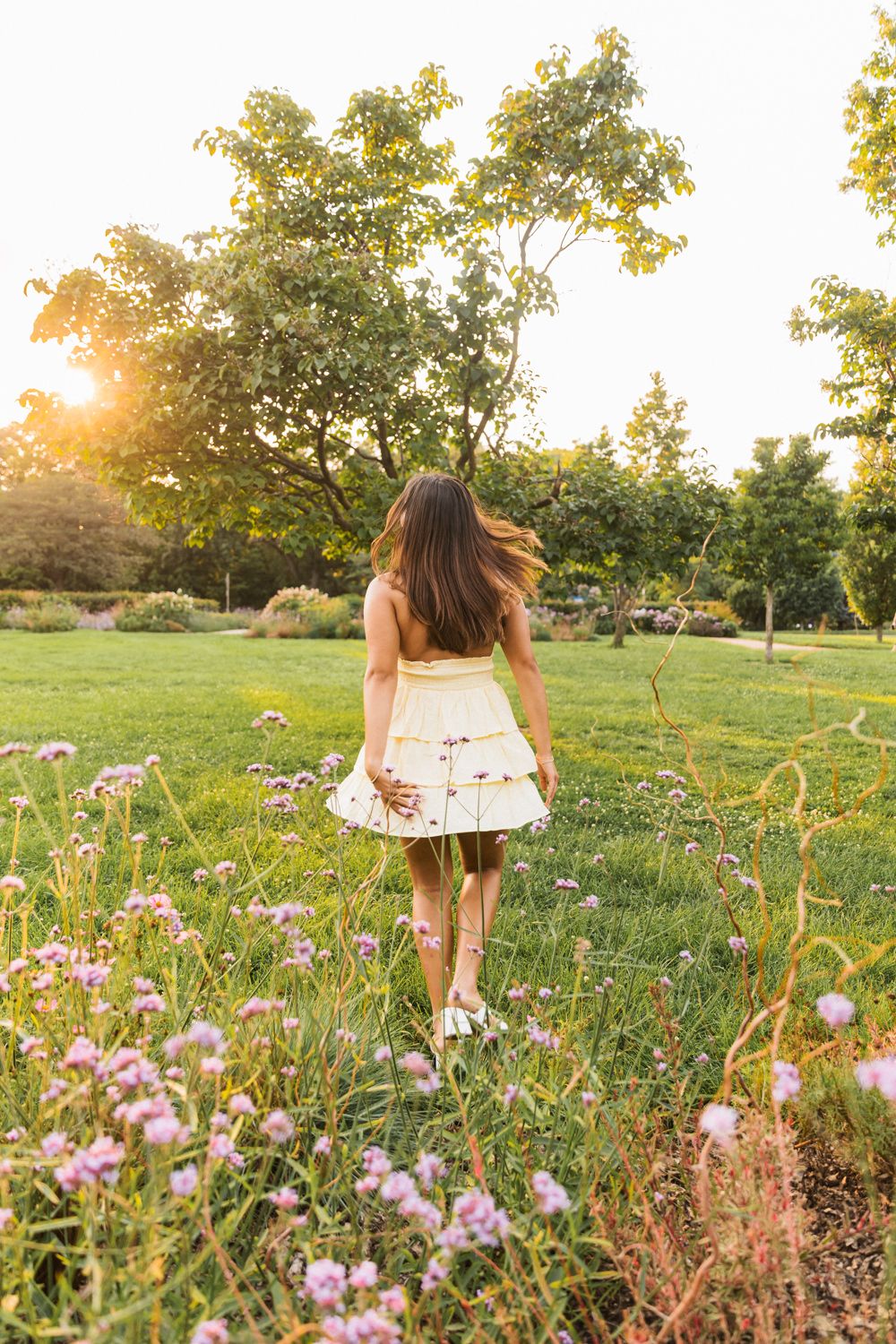 A dreamy scene in a wildflower meadow at golden hour with pink blooms and trees in the background.