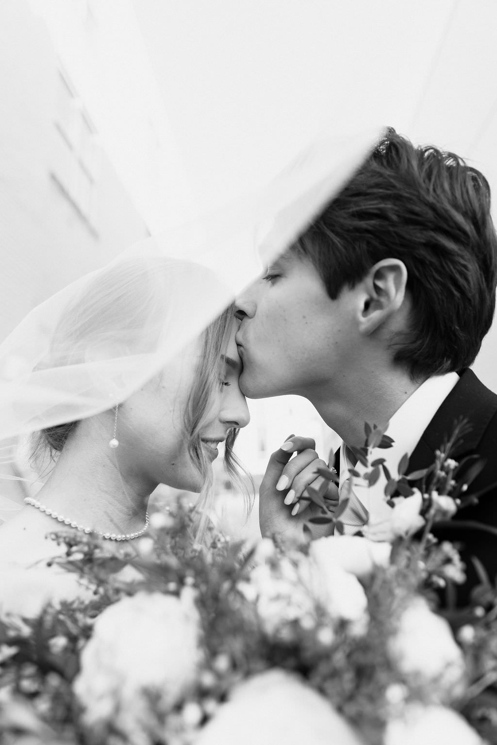 Black and white romantic wedding photo sequence showing couple under veil with flowers in soft focus.