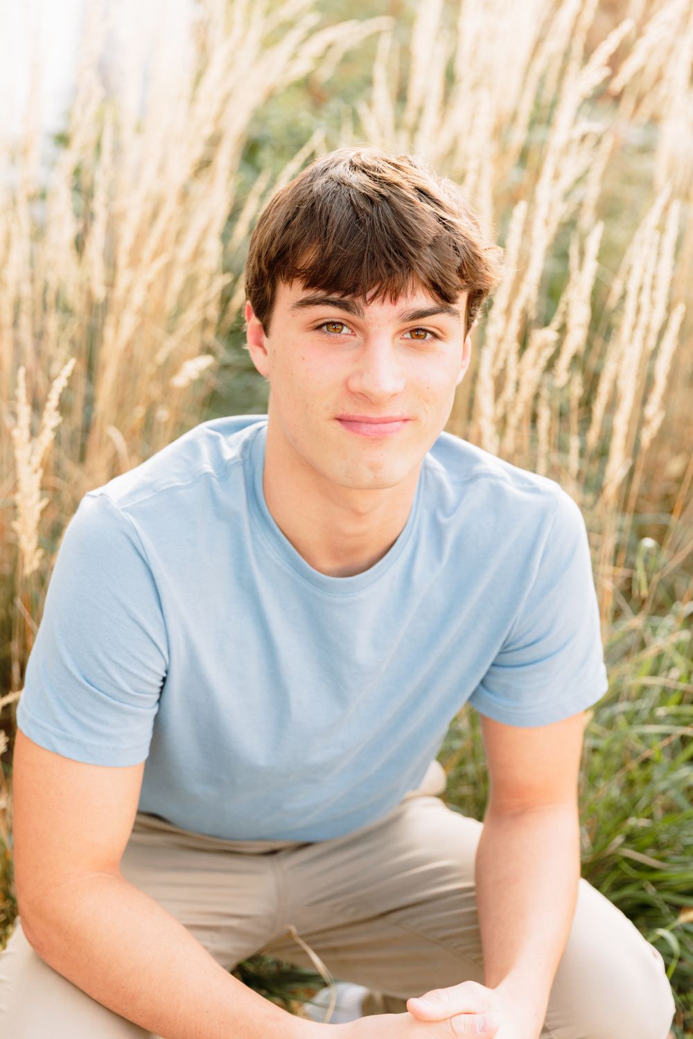 Casual portrait against tall grass wearing light blue t-shirt and khaki pants in natural outdoor setting.