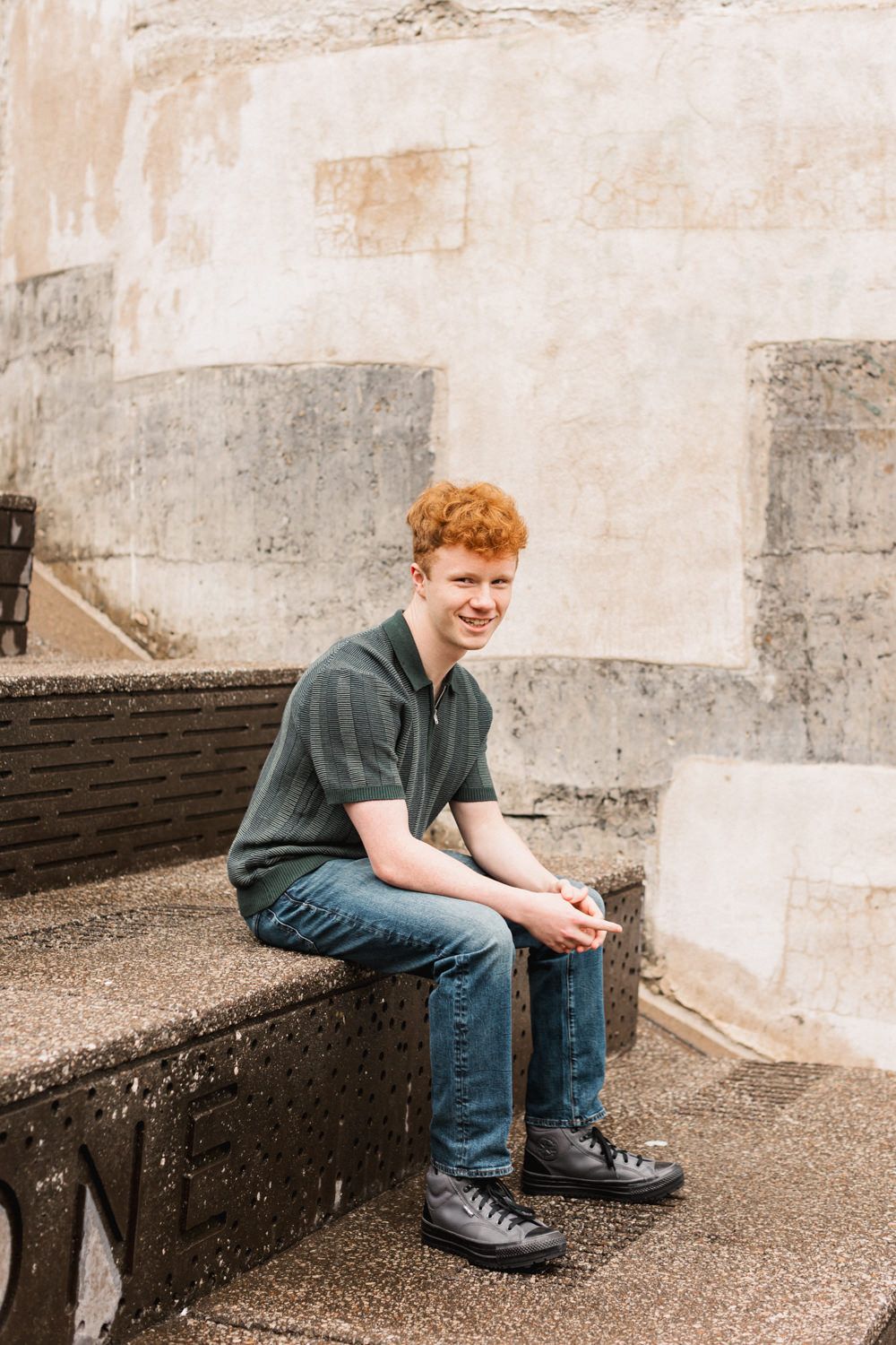 Person wearing blue denim and dark shoes sits contemplatively on concrete bench in urban setting.