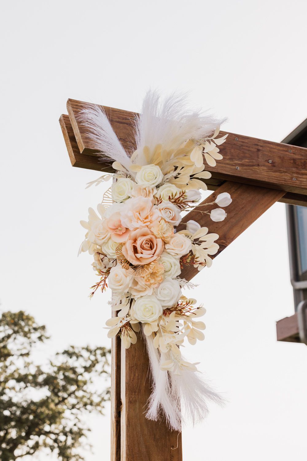 Wooden wedding arch decorated with elegant pink roses, white feathers and delicate floral arrangements.