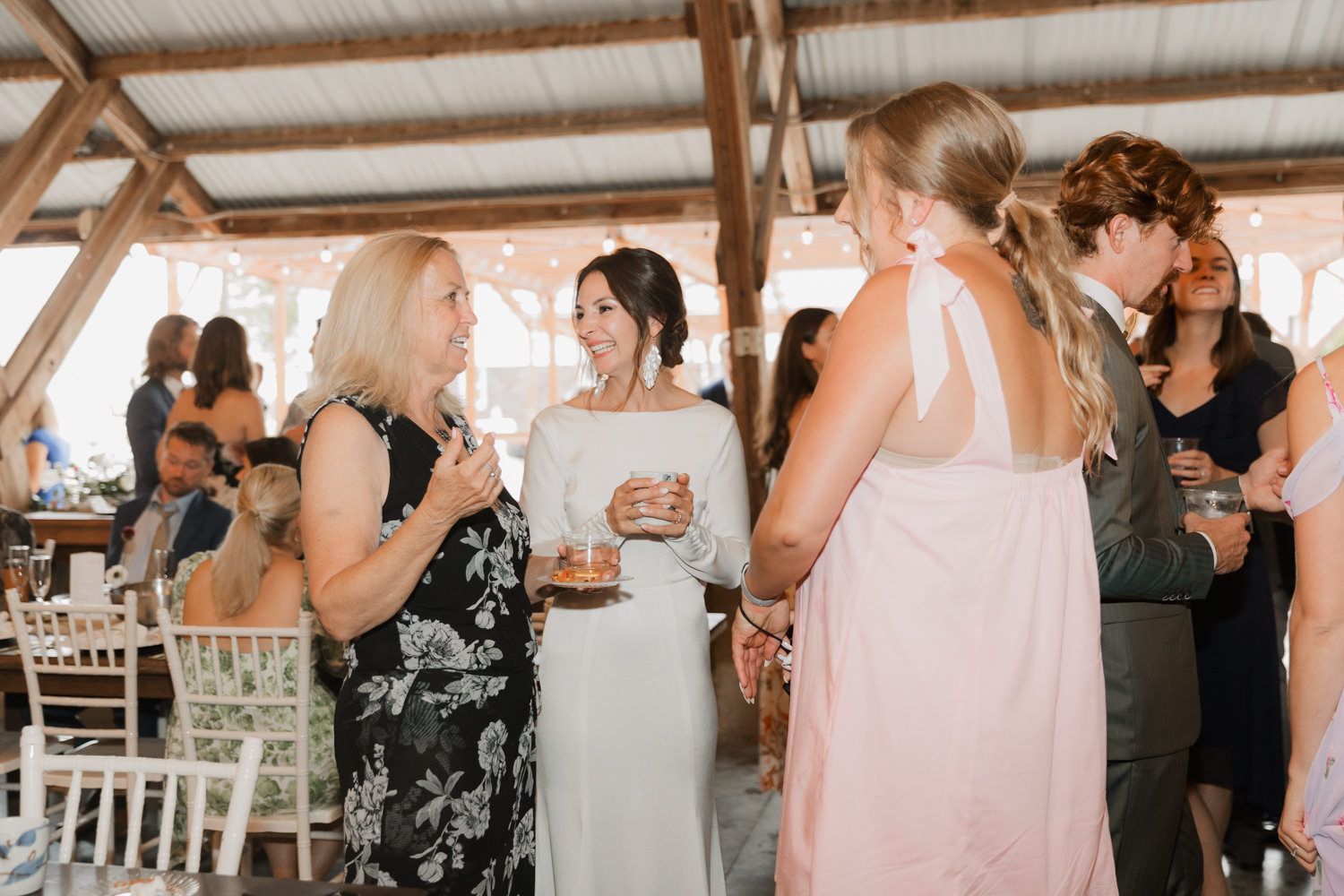 Wedding guests socializing during reception in an elegant barn venue with white chairs.