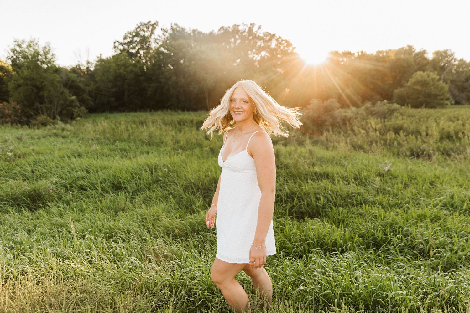 A person in a white dress spins joyfully in a sunlit green field during golden hour.