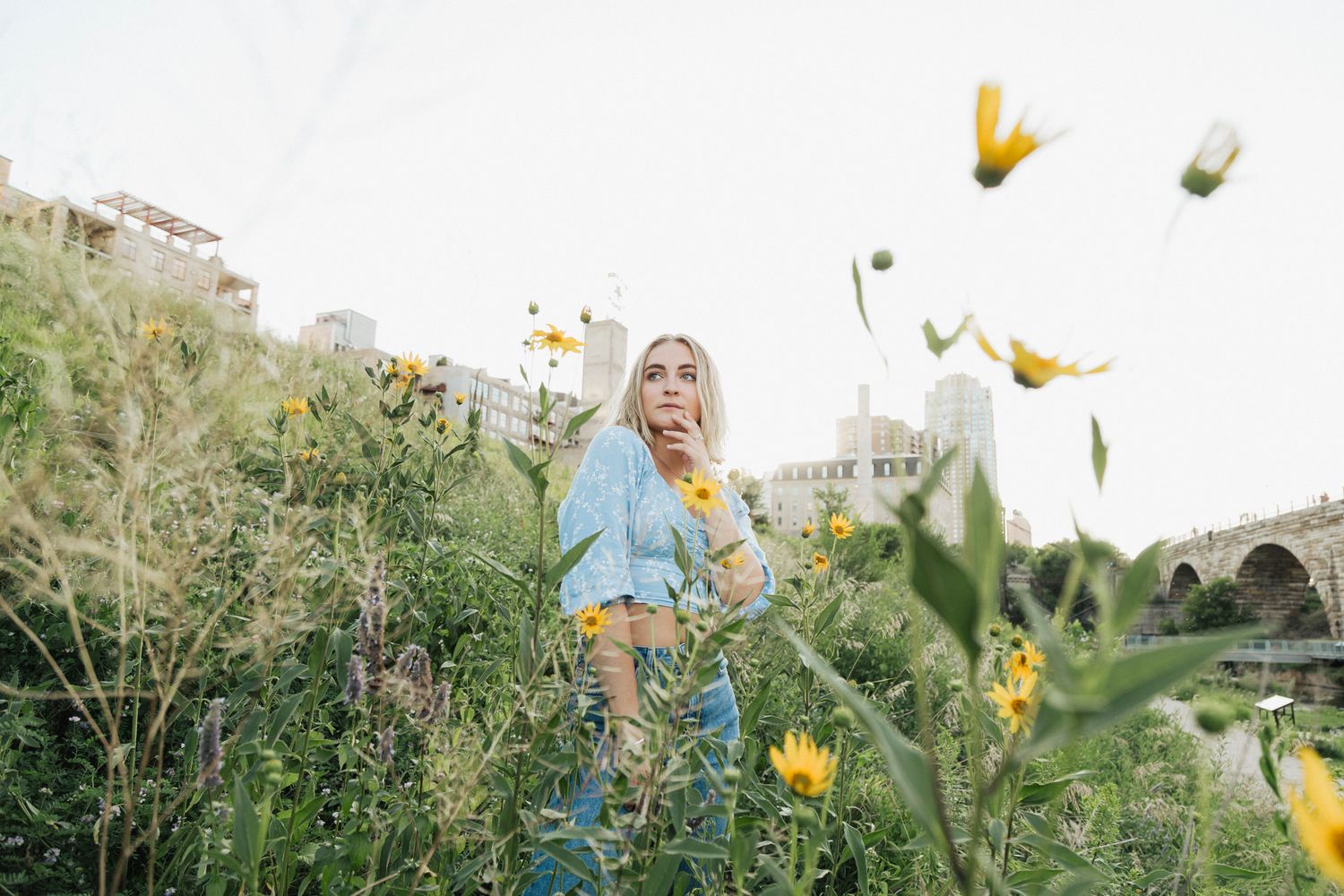 Ethereal outdoor portrait among yellow flowers and wild grass in an urban garden setting.