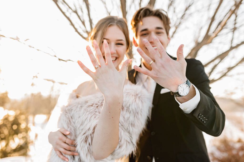 Wedding couple shows off their rings in outdoor winter engagement photo shoot.
