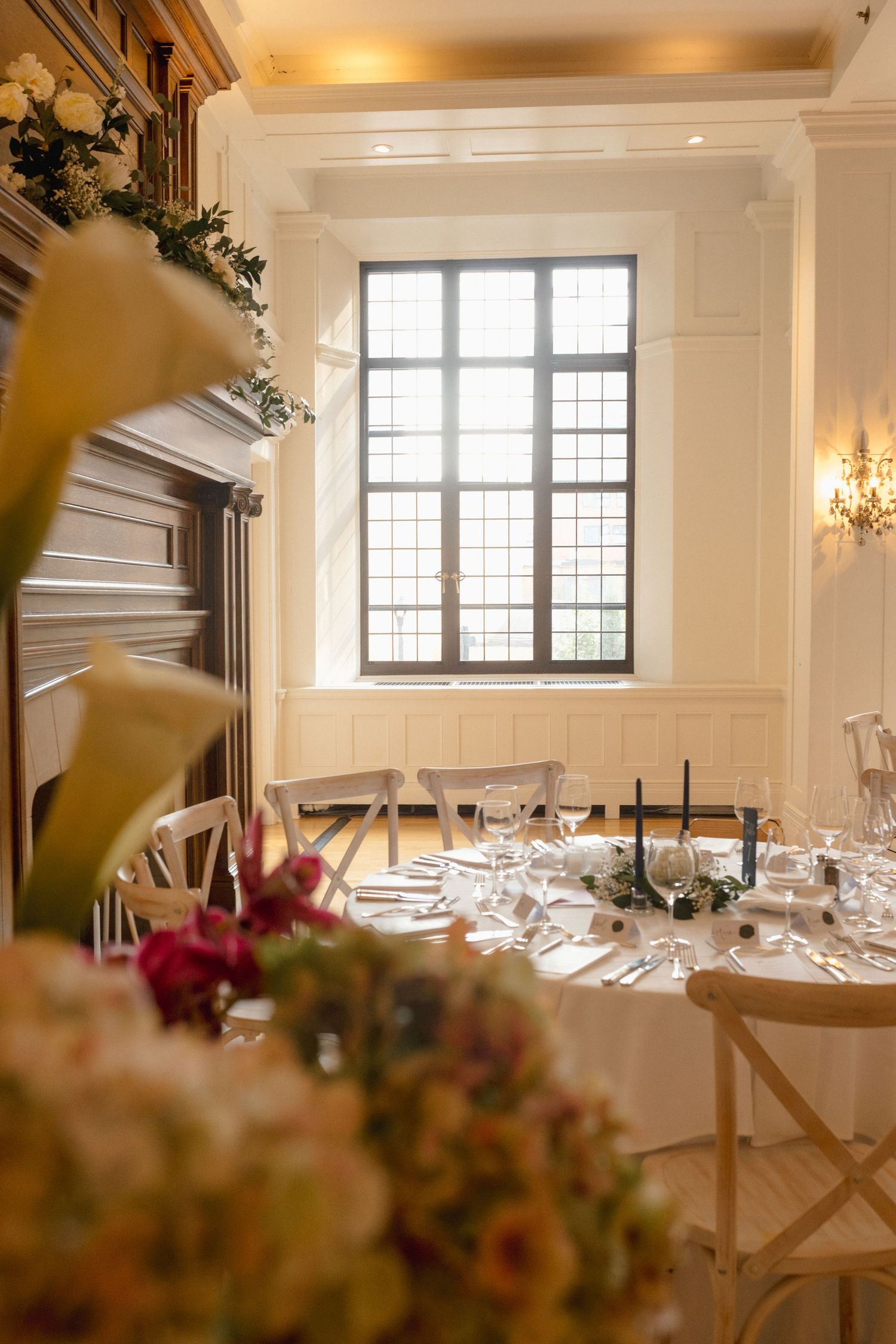 Elegant wedding reception table setting with black candles, floral centerpieces, and leaded glass windows in a classic venue.