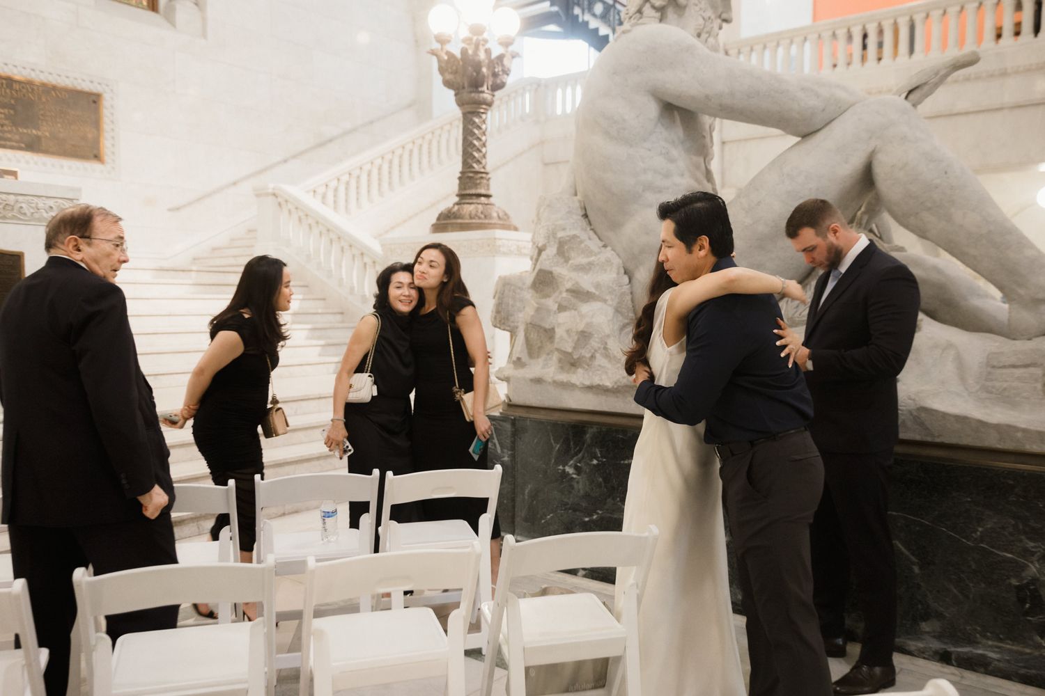 Elegant wedding reception in a grand hall with guests congratulating the newlyweds near a marble staircase and sculpture.