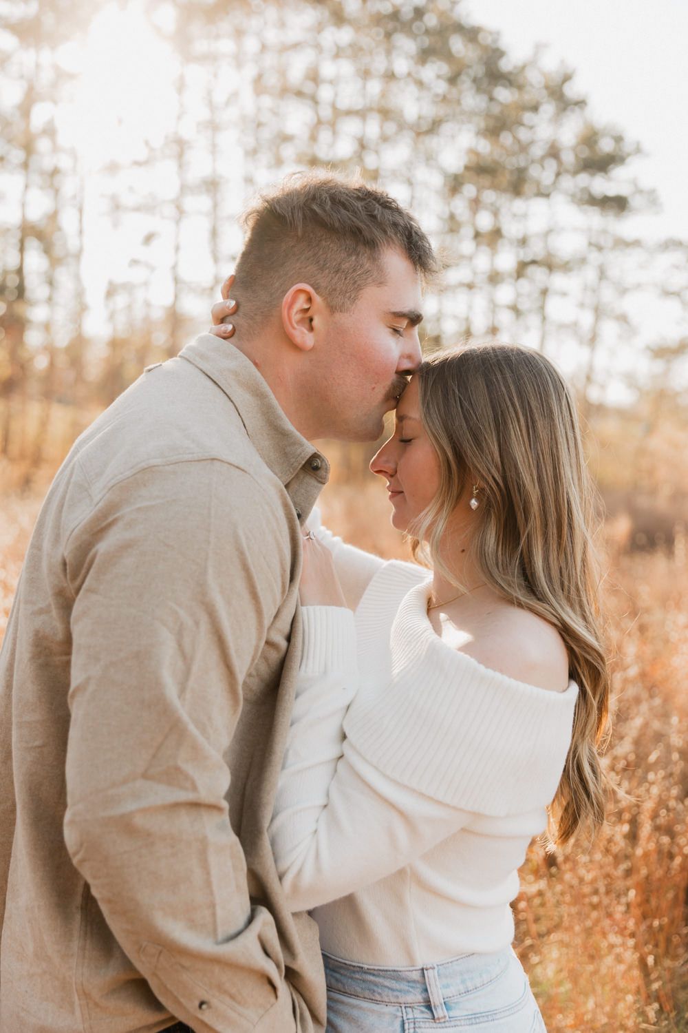 A couple shares an intimate moment while embracing in a sunlit forest with golden fall colors.