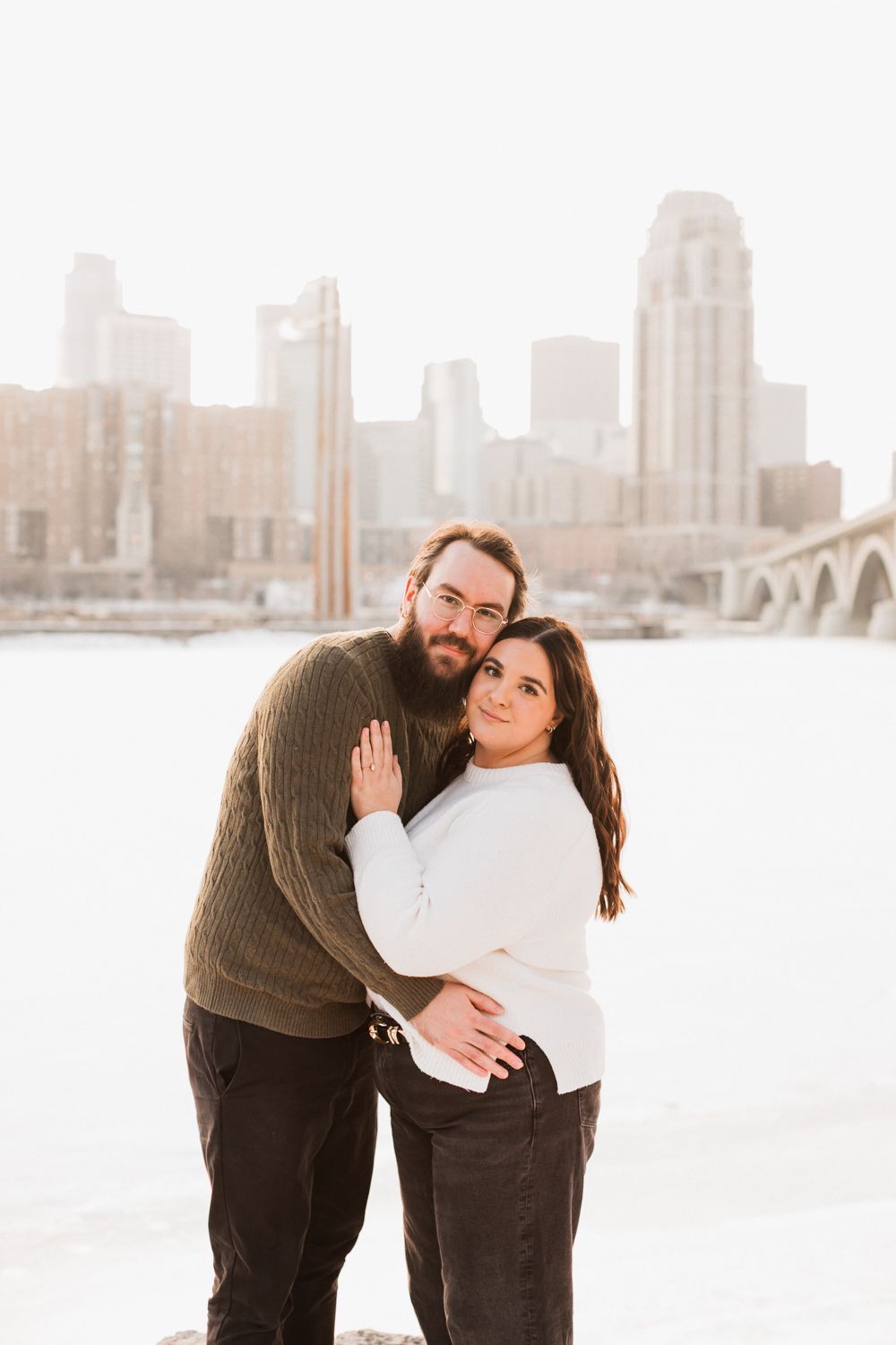 A couple shares romantic moments in front of a city skyline on a bright winter day.