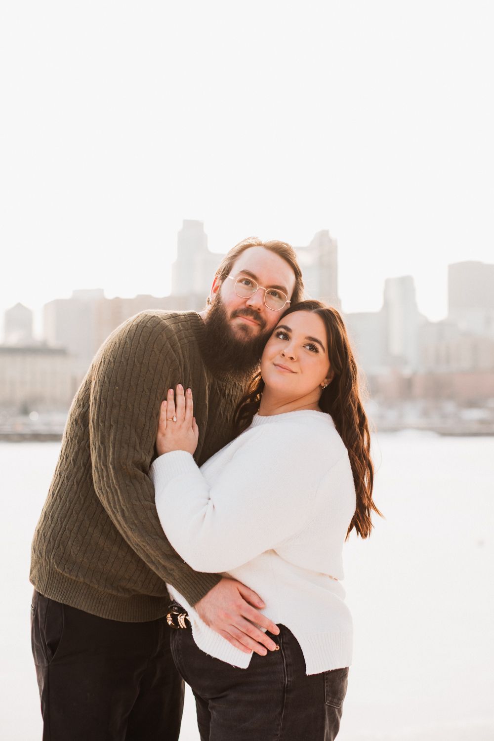 A couple shares intimate moments together against a bright cityscape backdrop in winter.